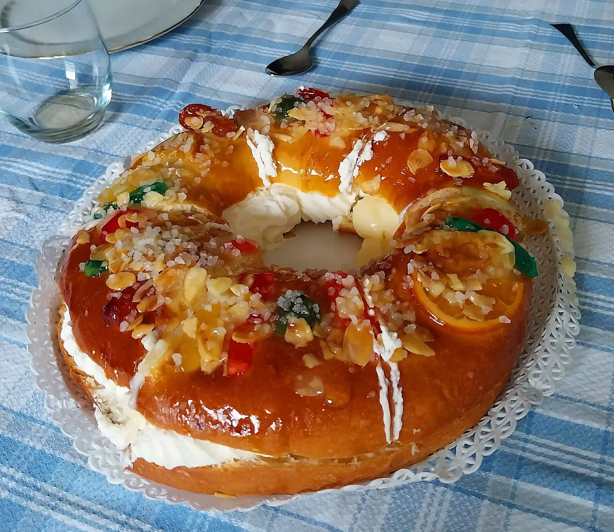 Roscón de Reyes con fruta confitada y almendra laminada sobre un mantel de cuadros azules