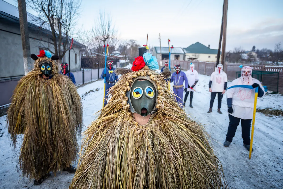 Malanka mummers in straw costumes and masks on a snowy village street in Ukraine