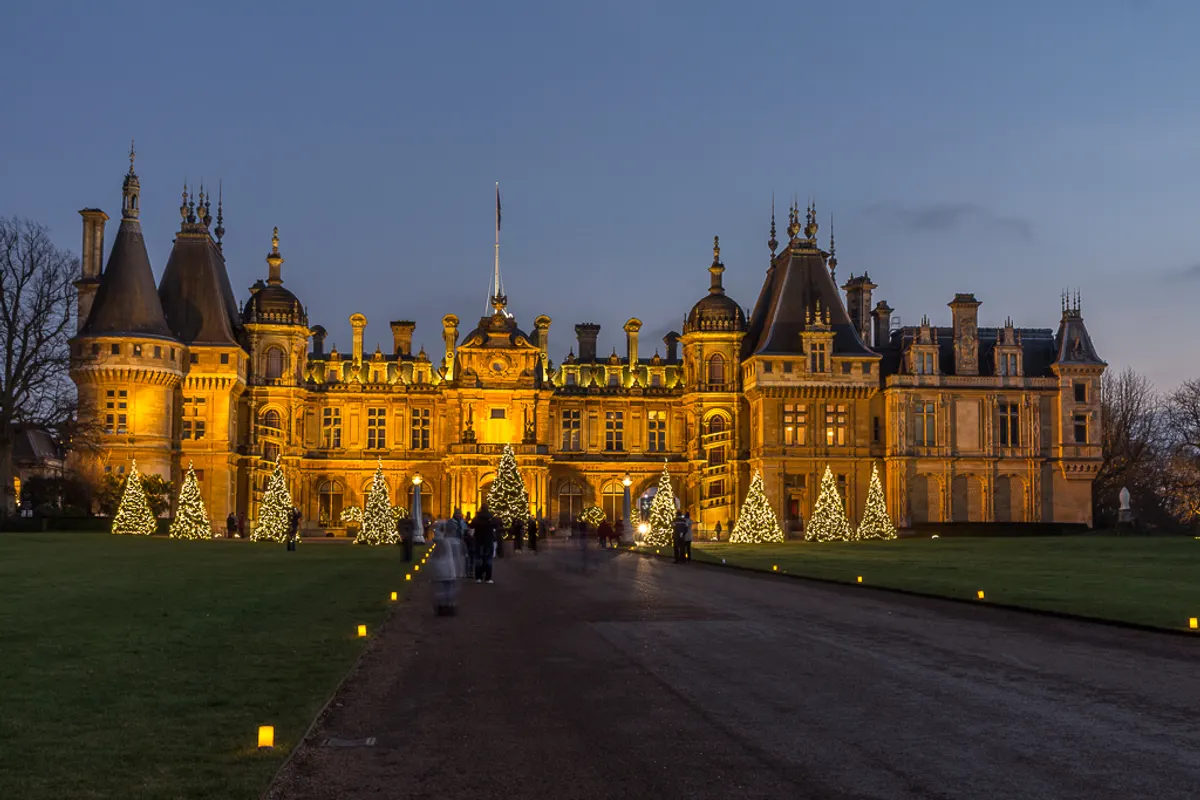 Waddesdon Manor glowing at dusk with lit Christmas trees on the lawn