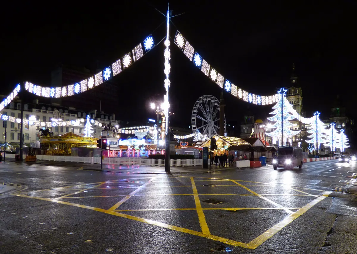 Arches of Christmas lights across a Glasgow city centre street with the big wheel behind