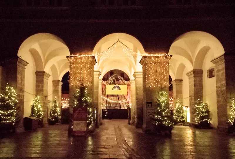 Beleuchteter Arkadengang mit Tannenbäumen beim Salzburger Christkindlmarkt am Abend