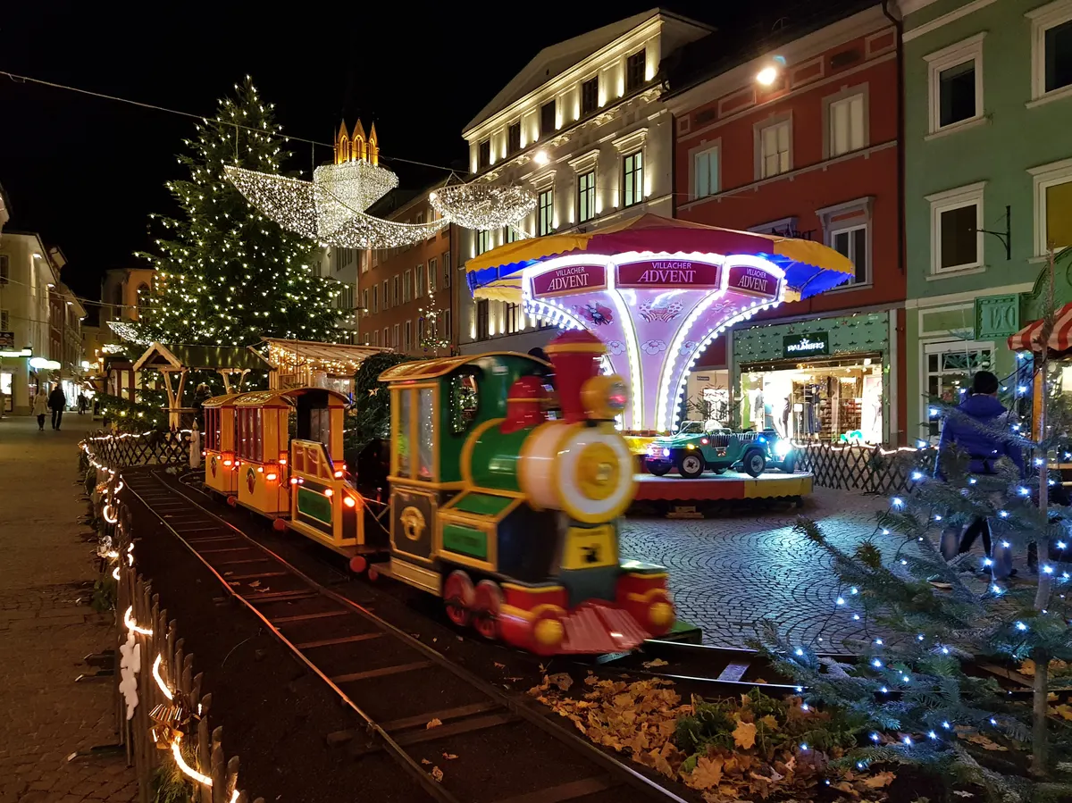 Christbaum, Kinderbahn und Lichter beim Villacher Advent am Abend