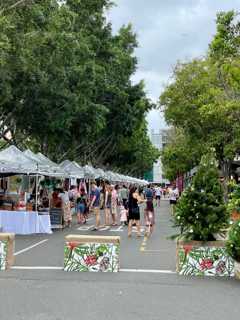 Shoppers browsing summer Christmas market stalls under trees in South Brisbane