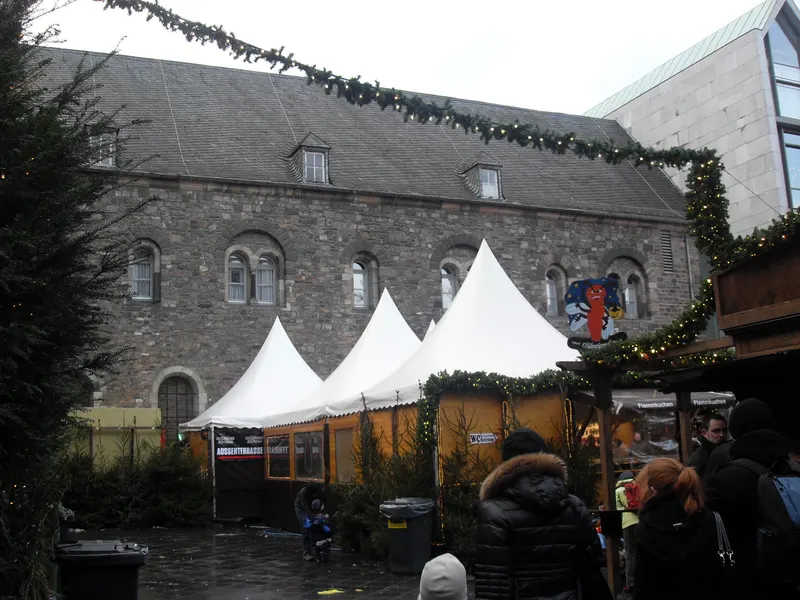Weiße Zelte und Girlanden vor einer Steinmauer auf dem Aachener Weihnachtsmarkt