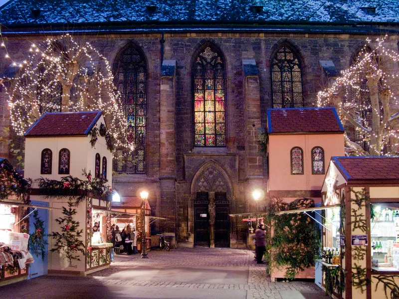 Chalets illuminés devant l'église Saint-Matthieu au marché de Noël de Colmar