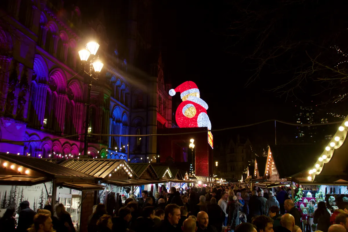 Crowds among the wooden chalets with the giant illuminated Santa at the Manchester Christmas Markets