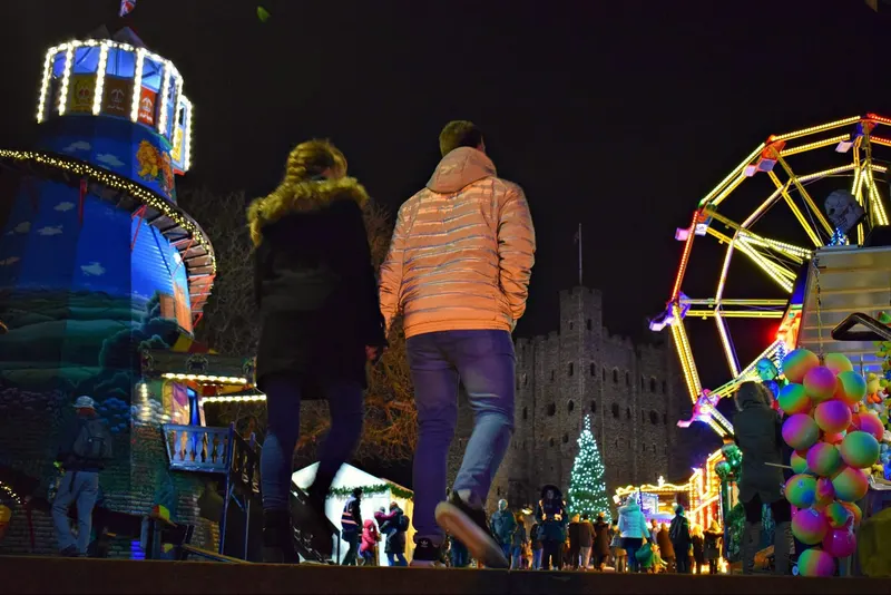 Visitors walking past funfair rides at Rochester Christmas Market