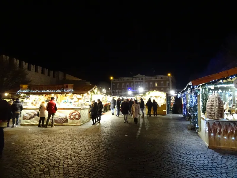 Viale di casette illuminate ai Mercatini di Natale di Trento di notte