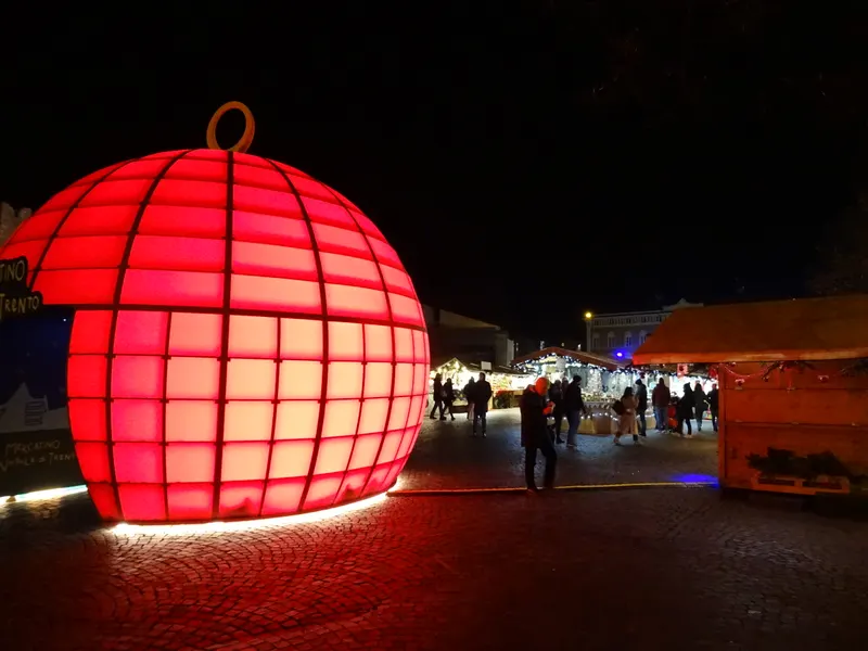 Grande palla luminosa rossa tra le casette dei Mercatini di Natale di Trento