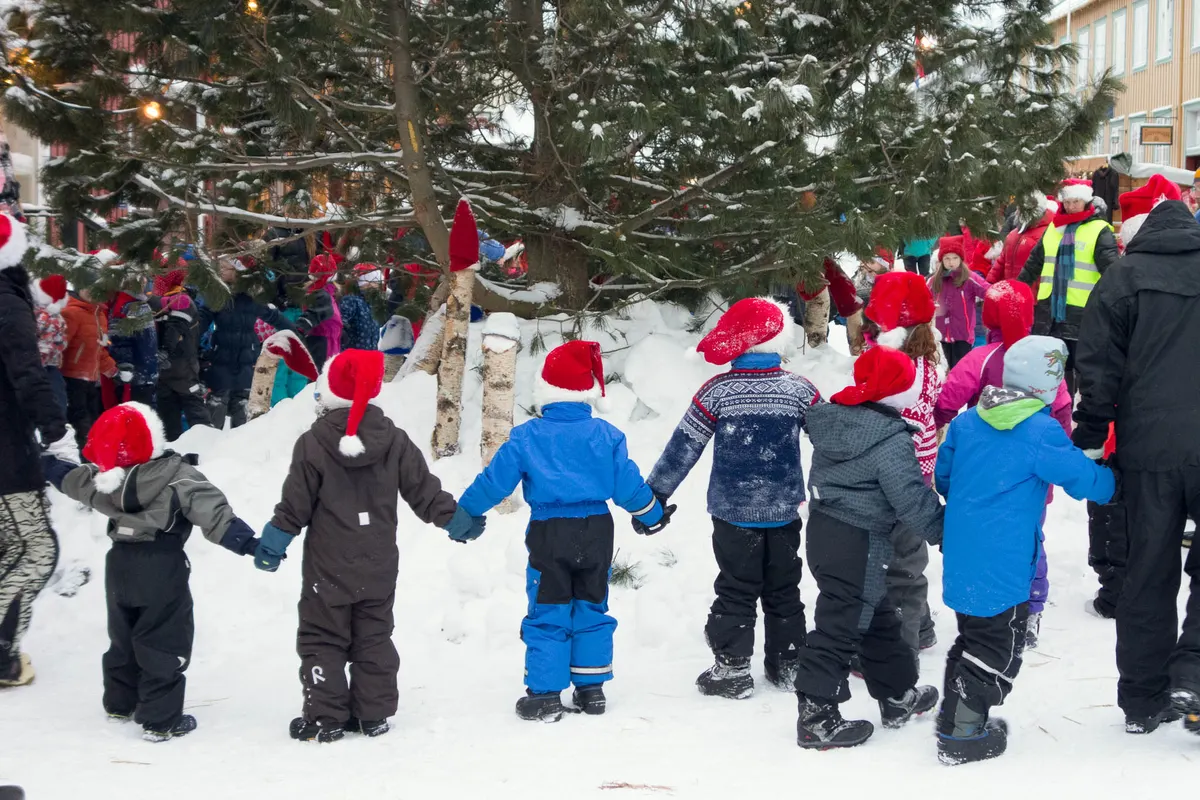 Barn med nisseluer danser rundt juletreet i snøen i Røros