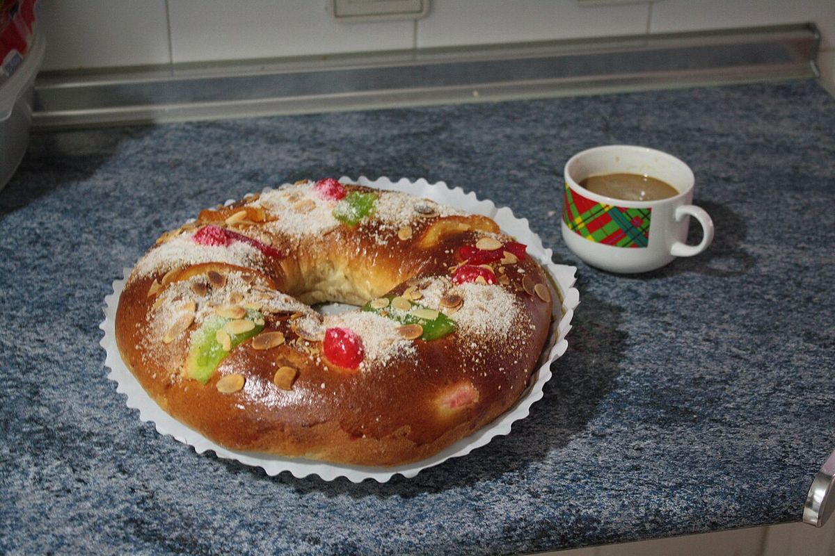 Roscón de Reyes con fruta escarchada y almendra laminada, junto a un café
